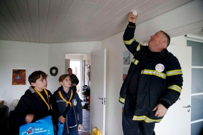 Brandmand Alex Langelund Iversen fra Brand & Redning MidtVest monterer en røgalarm, mens Carl Farcinsen, t.v., og Johan Odsbjerg Wach fra 1. Hede DDS ser til. Deres blå tasker er fulde af røgalarmer, batterier, brochurer og klistermærker. Røgalarmer skal helst sidde, der hvor man sover, og er der både loft og kælder, bør der også være alarmer der. I dag kan man ovenikøbet købe serieforbundne røgalarmer, fortæller Alex Langelund Iversen. ?Foto: Flemming Hansen