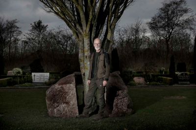 Hans Tølbøl har i 36 år arbejdet som graver ved Haderup Kirke, men besluttede for nyligt at gå på pension. Her står han foran en skulptur, som han er idémanden bag. Stenen, der symboliserer døden, bliver gennembrudt af træet, som symboliserer livet eller Kristus. Foto: Henrik Ole Jensen