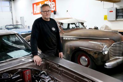 Per Andersen med firmabil Buick Special fra 1941 i baggrunden. Han vil ikke føre den tilbage i oprindelig tilstand med sort lak og gråt tag, men lade den stå, som den er.