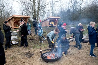 Nybagte boller og chili sin carne var festmenuen, da to nye shelters blev indviet ved Holtbjerg Sø på en våd dag. Naturvejleder Karen-Louise Smidth med de gule handsker bagte bollerne over åben ild. Hun glædede sig over det tværfaglige projekt, der har gjort de to shelters mulige. Det gør det nemmere at hente hjælp og kompetencer hos hinanden næste gang, der er et projekt, som skal søsættes, sagde hun. Det bliver dog ikke med hende som deltager. Hun stopper efter syv et halvt år som naturvejleder i Herning Kommune, da hun har fået nyt arbejde i byrådssekretariatet i Billund Kommune fra 1. februar. ?Foto: Tom Laursen
