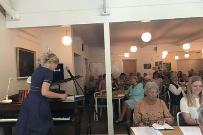 Stemningsbillede fra Højskolen Skærgården, hvor sognepræst Inge Marie Kirketerp (t.v.) er ved at finde næste sang, inden hun spiller ved klaveret. I forgrunden midt for sidder Bitten Damgaard, der er formand for højskolen. Bitten Damgaard er også tovholder på udvalgte sange og idékvinde bag hele konceptet, som blev holdt for tredje gang.