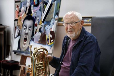Musikken og maleriet. Per Jegbjærg spiller med basunen en central rolle i både det Herningbaserede hyggeorkester The Band og det professionelle Bourbon Street Jazzband, hvor han har været medlem i godt 35 år. Derudover har han siden seminarietiden på Herning Seminarium dyrket billedkunsten. Bag ham i det lyse atelier ses det seneste maleri »Das Kapital« med ansigter fra Børsen i New York (og en lille Joakim von And, der humoristisk har sneget sig ind i et hjørne). Foto: Henrik Ole Jensen henrik ole jensen