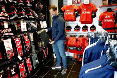 FC Midtjyllands merchandise-chef, Tommy Pedersen, blandt de farvestrålende produkter i »Ulveshoppen« på MCH Arena. Her må kunderne fremover indstille sig på et farvel til plasticposer og goddag til en lidt dyrere papirspose, når varerne skal med hjem. Foto: Henrik Ole Jensen