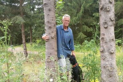Peter Benfelt - og hunden Karla - giver to grantræer et kram. Træerne står i hans lille skov og binder et ton CO2 og giver deres bidrag til at forsinke klimaforandringerne. Peter Benfeldt mener, at lovgiverne bør åbne for, at der plantes endnu mere skov for miljøets skyld. Foto: Jesper Wind