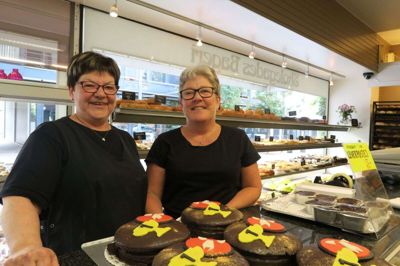 Butikspigerne Berit Frifeldt Hansen (t.v.) og Jane Bentsen (t.h.) griner og spøger med hinanden, mens de langer mesterskabskager og rundstykker over bagerdisken fredag morgen.