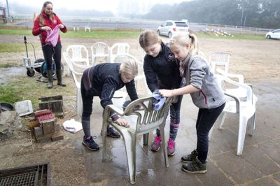 Hvide plastikstole bliver vasket klar, så forældrene siddende og med afstand kunne kigge med til rytterlejrens afsluttende springstævne. Foto: Tom Laursen