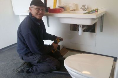 Lars Christensen lægger sidste hånd på det nye toilet ved »Rimmerhus«. Projektet med fælleshus, shelter, toilet, udeløkken og legeplads har fået støtte fra flere puljer og fonde. Lars Christensen fremhæver de lokale håndværkere, der har hjulpet til ved at give gode tilbud. Foto: Jesper Wind