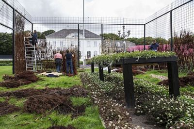 Et fem meter højt hegn af armeringsjern bliver beklædt med skræpper. Midt i det hele står et kæmpe bord dækket op med blomster. Foto: Jørn Deleuran