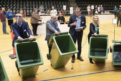 De grønne beholdere vises frem, som valgloven påbyder, og de konstateres ganske tomme. Umiddelbart efter dumper de første stemmer ned i det grønne dyb. Foto: Tom Laursen