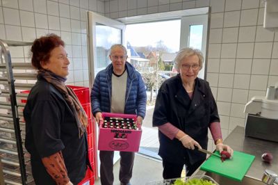 Liv Serup (t.v.) er frivillig koordinator på Café Møltrup i Videbæk. Hun leder 18 frivillige og her kigger hun Margit Andersen over skulderen, men hun lige snitter lidt salat og Laurits Østergaard har hentet en kasse sodavand til kølerummet. Foto: Jens Kristian Lynderup