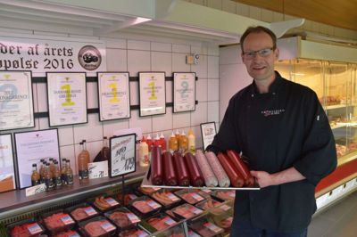 Ejstrupholms slagterbutik fik for 20 år siden lagt en naboforretning til, så der er kommet et baglokale. Det gør, at der er plads til at producere flere varer selv - som de pølser, Claus Laursen her står med. Foto: Michael Holmgaard Christiansen