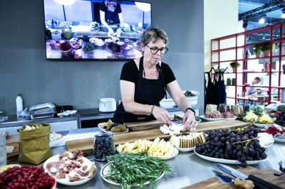 Mens ostekommunikatør Camilla Bojsen-Møller anrettede sit ostebræt med de elementer, hun havde klargjort, kunne tilhørerne følge med på skærm og køkkenbord. Hun driver sitet »ostesnak.dk«, hvor hun minder besøgende om; »don’t worry, brie happy«. Foto: Tom Laursen