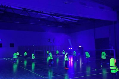 Natminton spilles i en mørklagt hal med selvlysende tape på gulvet, selvlysende veste og selvlysende fjerbolde - men reglerne er de somme som til almindelig badminton. Foto: Michael Wiese