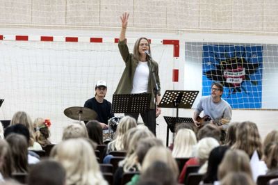 Inger Lene Krath Pedersen, musiklærer på Brændgårdskolen, styrer korsangen fra scenen og får eleverne til at synge med på »Jungledyret Hugo.« Foto: Tom Laursen