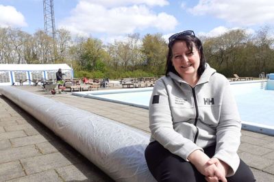 Dorthe Kring på den nye måtte, der skal rulles ud over bassinet i Ilskov Friluftsbad. I baggrunden er det Bent Boesen. Han er ansat af landsbyen til at holde de grønne områder. Ilskov leder også med lys og lygte efter en køkkendame, der kan hjælpe friluftsbadet og Ilskov-Hallen. Foto: Jesper Wind