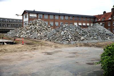 De store bunker med byggeaffald fra den tidligere psykiatriske afdeling ligger stadig på byggepladsen ved Skolegade, og nedrivningen af bygningen bag ved er ikke for alvor kommet i gang. Sådan har det set ud siden sensommeren sidste år, og det er to naboer ved at være trætte af at kigge på. Foto: Chresten Bergh