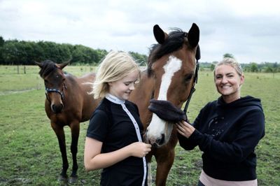 Datter og mor går begge op i heste. Her er de fotograferet ved Katarina Dam Jensens hest, Mercedes, som har fået trukket en tand ud, så den skal ikke deltage i stævnet. Det skal 11-årige Silke Dam Jensen, der skal deltage i spring med Lamezia, der ses bagved. Foto: Chresten Bergh