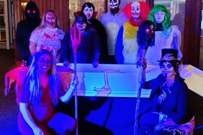 Fotoet fra artiklen i mandagsavisen. Det viser det uhyggelige halloween-hold fra 2022 flankeret af Jan Birk Knudsen, chefen i Vores Ikast, som ses med røde, onde øjne yderst til venstre.