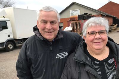 Anna og Hilmer Lyhne foran det firma, Hilmer Lyhne oprettede i 1973 og som sønnen, Kristian Lyhne, driver i dag. I baggrunden holder den lastbil, som Hilmer Lyhne bruger, når han kører ud med træpiller.