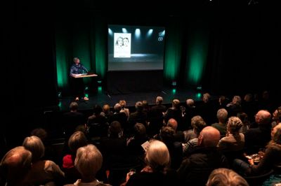 Michael Asmussen præsenterer forestillingen »Bag facaden« for en næsten fyldt sal.