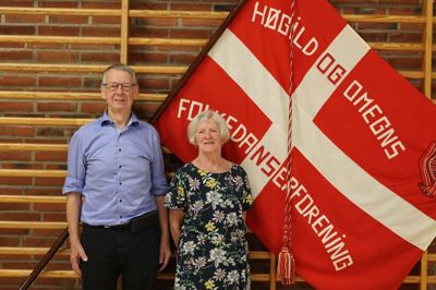 En formand og en pioner. Vang Flensborg er formand for Høgild og Omegns Folkedanserforening, som Aase Jensen var med til at etablere i 1975 og stadig danser i. En særlig detalje ved foreningens fane er folkedanserparret i øverste højre hjørne, som er sirligt håndbroderet af et tidligere medlem.