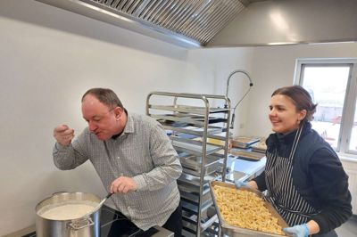 Friskoleleder Henrik Olesen får lov at smage på dagens skolemad til de yngste klasser på Aulum Kristne Friskole, som skolens madmor Anna Kathrine Lauridsen forbereder.