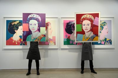 To kunstteknikere holder to portrætter af dronning Elizabeth II, som popartkunstneren Andy Warhol har skabt, op. Bag dem ses Warhols portræt af danske dronning Margrethe. To eksemplarer af værkerne kommer på auktion hos det danske auktionshus Bruun Rasmussen.