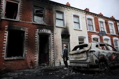 En kvinde står uden for en udbrændt hus i Belfast. Huset brød i brand i forbindelse med optøjerne tirsdag aften.