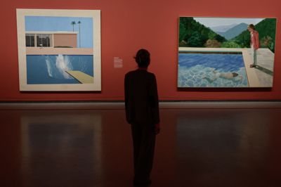 En museumsgæst betragter på et kunstmuseum i Paris malerierne »A Bigger Splash« (til venstre) og »Portrait of an Artist (Pool with Two Figures)« (til højre) af David Hockney. Sidstnævnte satte rekord på auktion i 2018.