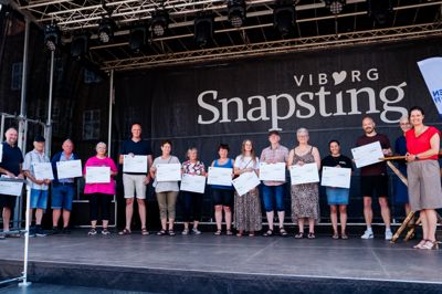 Repræsentanter fra de 15 deltagerbyer i Lokaldysten 2026 var på scenen sammen med borgmester Katrine Fusager Rohde (V) til højre.