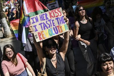 En demonstrant holder et skilt frem med teksten »I hendes kys kan jeg smage revolutionen« på gaden i Istanbul søndag. Myndigheder i den tyrkiske storby har i årevis forbudt LGBT-personer at holde prideparade eller på anden måde markere priden. Mange prøver alligevel, om de kan gennemføre en protest med krav om rettigheder til LGBT-personer.