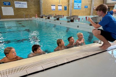 Instruktør Silas Bonde Christensen fortæller om næste programpunkt på svømmelejren i svømmehallen i Videbæk Idræts- & Fritidscenter.