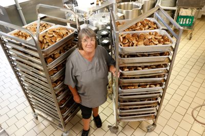Den erfarne køkkenleder Hanne Bech her blandt stabler af frikadeller i bakker, der skal varme op til 75 grader, puttes i varmekasser og leveres til Ramsing Cup. Hun tager det roligt og gør gerne arbejdet for, at Brejninggaard Efterskole kan bidrage til det gode samarbejde i lokalsamfundet.