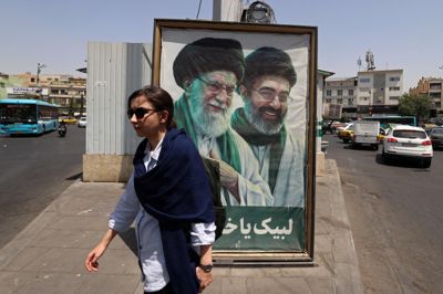 En kvinde går forbi et stort billede af Irans afdøde ayatollah Ali Khamaney, som ses til venstre, og hans søn, der er Irans nuværende øverste leder, ayatollah Mojtaba Khamanei, i Teheran 21. juli. Det er i øjeblikket »meget svært« at kommunikere med Mojtaba Khamenei, siger Irans præsident.