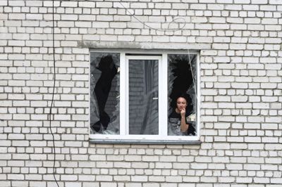 En kvinde kigger ud af et ødelagt vindue i en beboelsesejendom, som natten til fredag er blevet ramt i et russisk droneangreb i Kyiv.