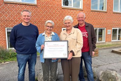Bestyrelsen for Multihuset i Klovborg blev hædret med Fællesskabsprisen 2026. Her er det fra venstre Morten Skovbo, Hanne Pedersen, Hanne Tønnesen Godskesen og Finn Schmidt, der fremviser prisen foran husets facade.