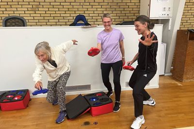 Solveig Kvåle Jensen gør sig klar til at prøve curling, mens Hanne Thisgaard og Jytte Thorup Jacobsen muntert iagttager hende. De tre kvinder er alle med til at få Aktivt Samvær i Ejstrupholm til at fungere.