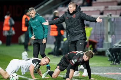 Cheftræner Mike Tullberg slår ud med armene, men Sofus Johannesen og St. Truidens Robert-Jan Vanwesemael er gået i græsset efter en duel.