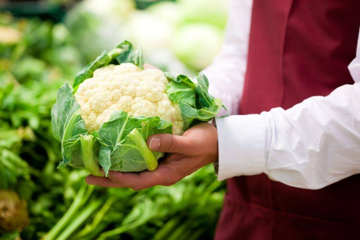 Man – only hands to be seen – in supermarket as shop assistant; he is carrying a cauliflower