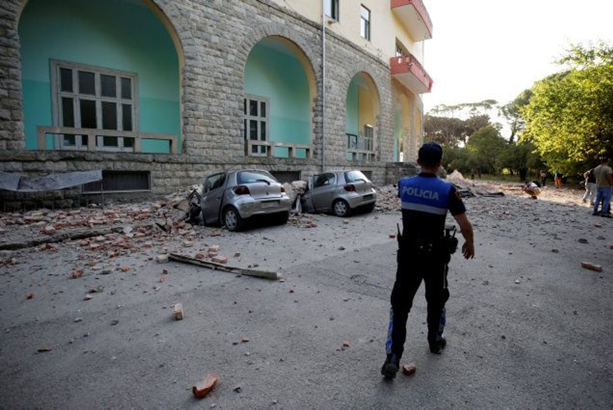 En politimand går forbi to beskadigede biler og en delvist ødelagt bygning i hovedstaden Tirana, der lørdag eftermiddag blev ramt af et jordskælv. Foto: Florion Goga/Reuters