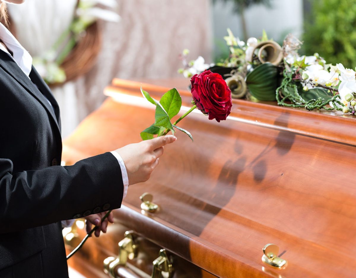 Mourning woman on funeral with red rose standing at casket or coffin