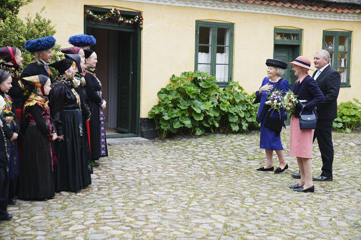 Dronningen og en tydeligt benovet prinsesse Beatrix betragter en gruppe mennesker i farvestrålende folkedragter.