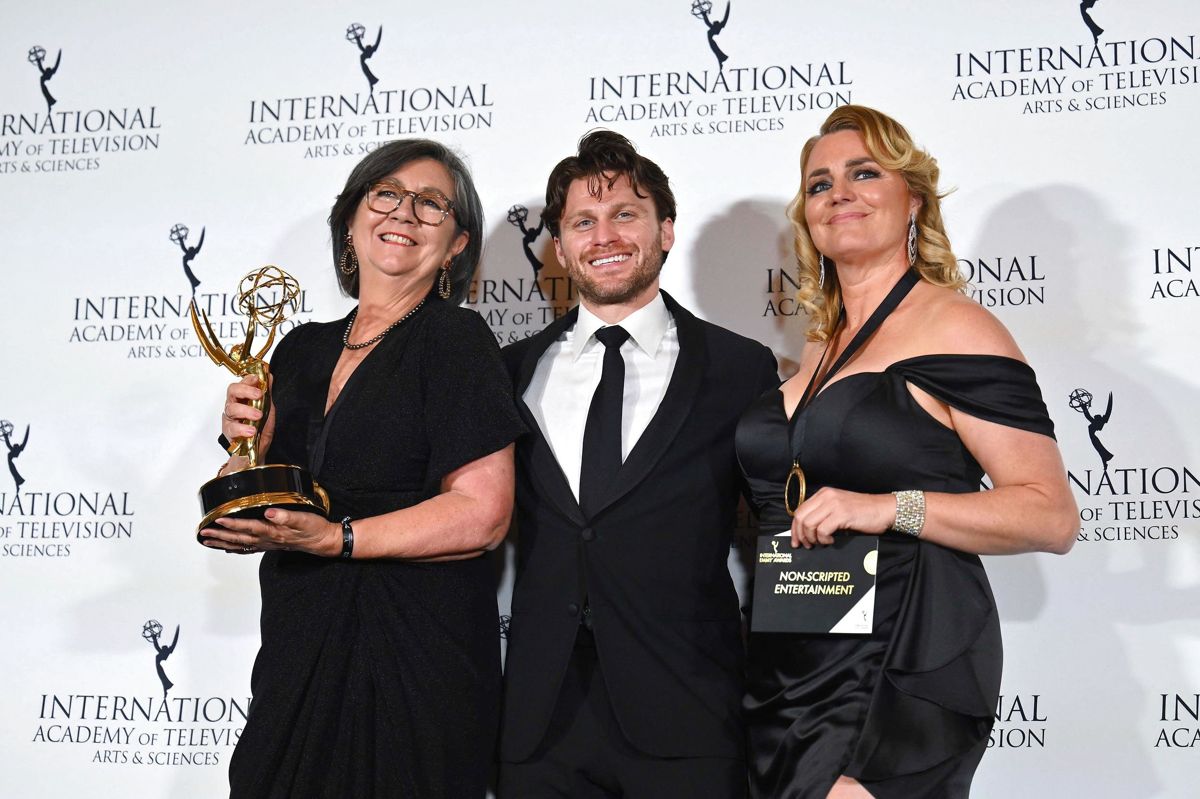 Karin Holden og Jenni Wilks poserer med den statuette, som de natten til tirsdag vandt for serien "Love on the Spectrum" ved International Emmy Awards i New York. Mellem dem ses skuespiller Jon Rudnitsky.
