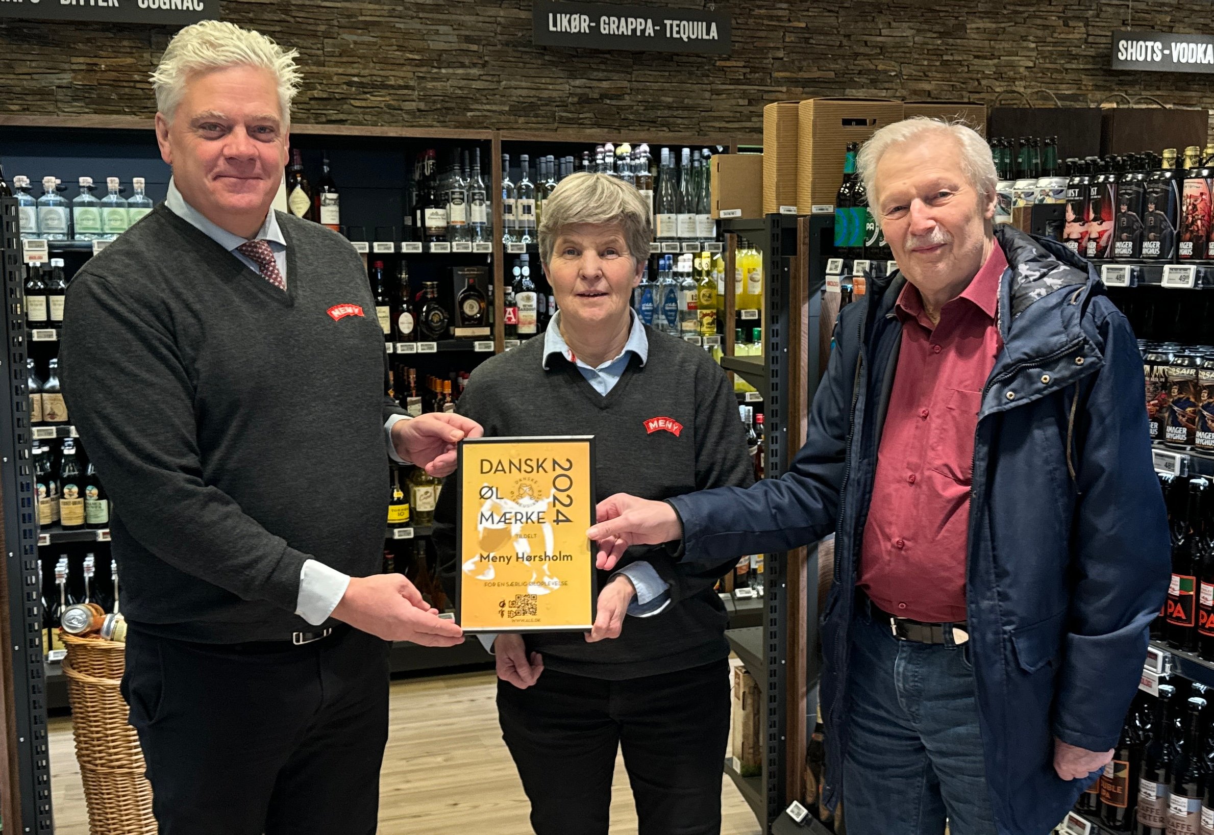 Købmand og indehaver af Meny Dalgaard, Lasse Simonsen (tv.), får med sin ølsommelier Dorte Jørgensen overrakt “Dansk Øl Mærke 2004” af formanden for Danske Ølentusiaster, Bjarke Christensen. Foto: Presse