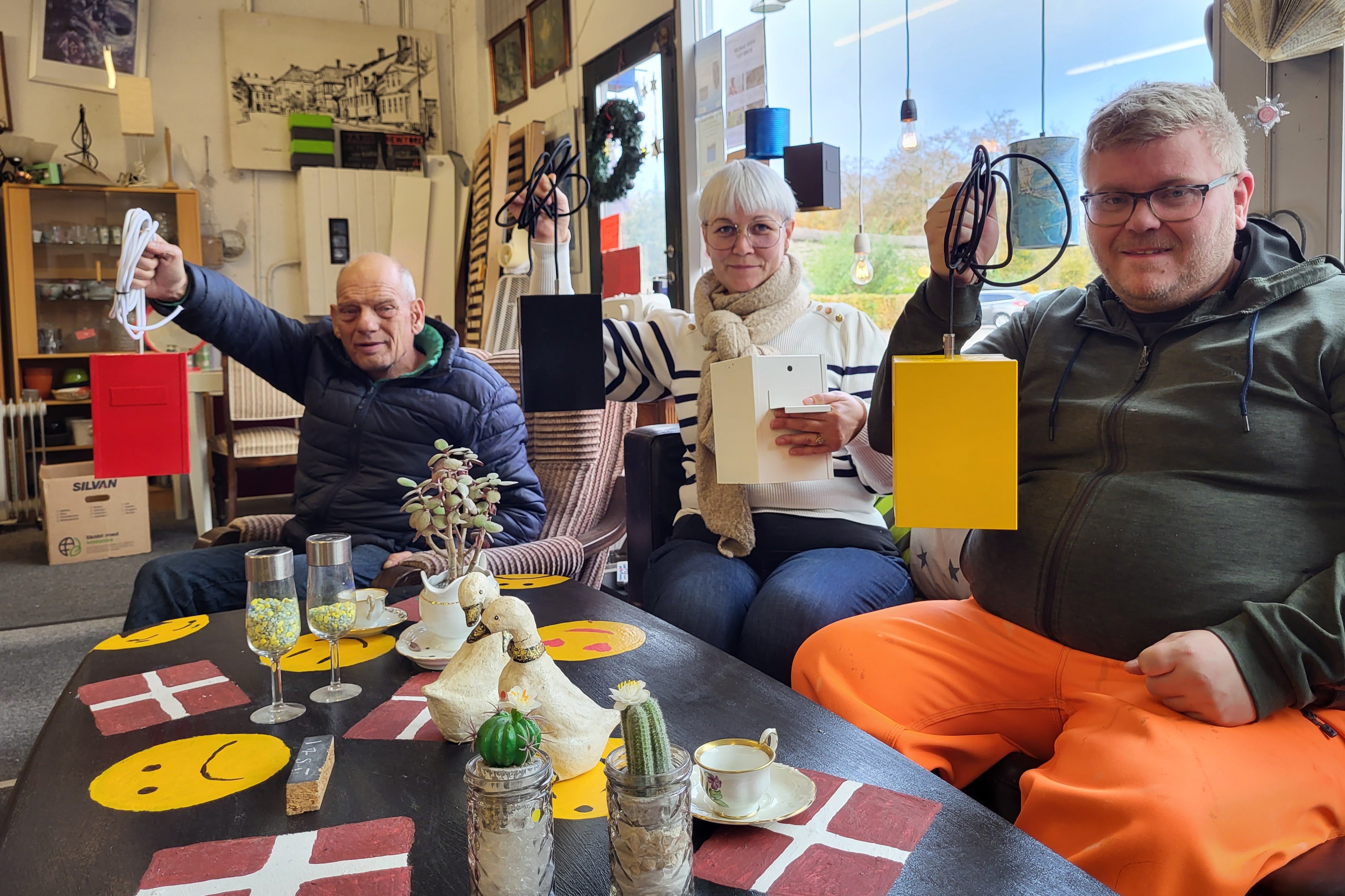 Flemming Holst og Michael Jensen har været med til at skille de originale lamper ad og vælge farver til de upcyclede lamper. Leder af Hot Skrot i Højby, Dorte Ryttergaard, viser også den originale hvide lampe frem. Foto: Pipaluk Balslev