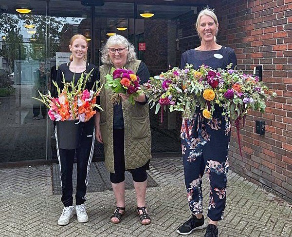 Erhvervspraktikant hos Krukkerne Liva Gerssø Jacobsen (t.v.) og Krukkernes indehaver, Karna Lønne, der også er formand for Allerød Handelsforening, afleverer blomster til Lene Irlind fra Engholm Plejecenter. Privatfoto
