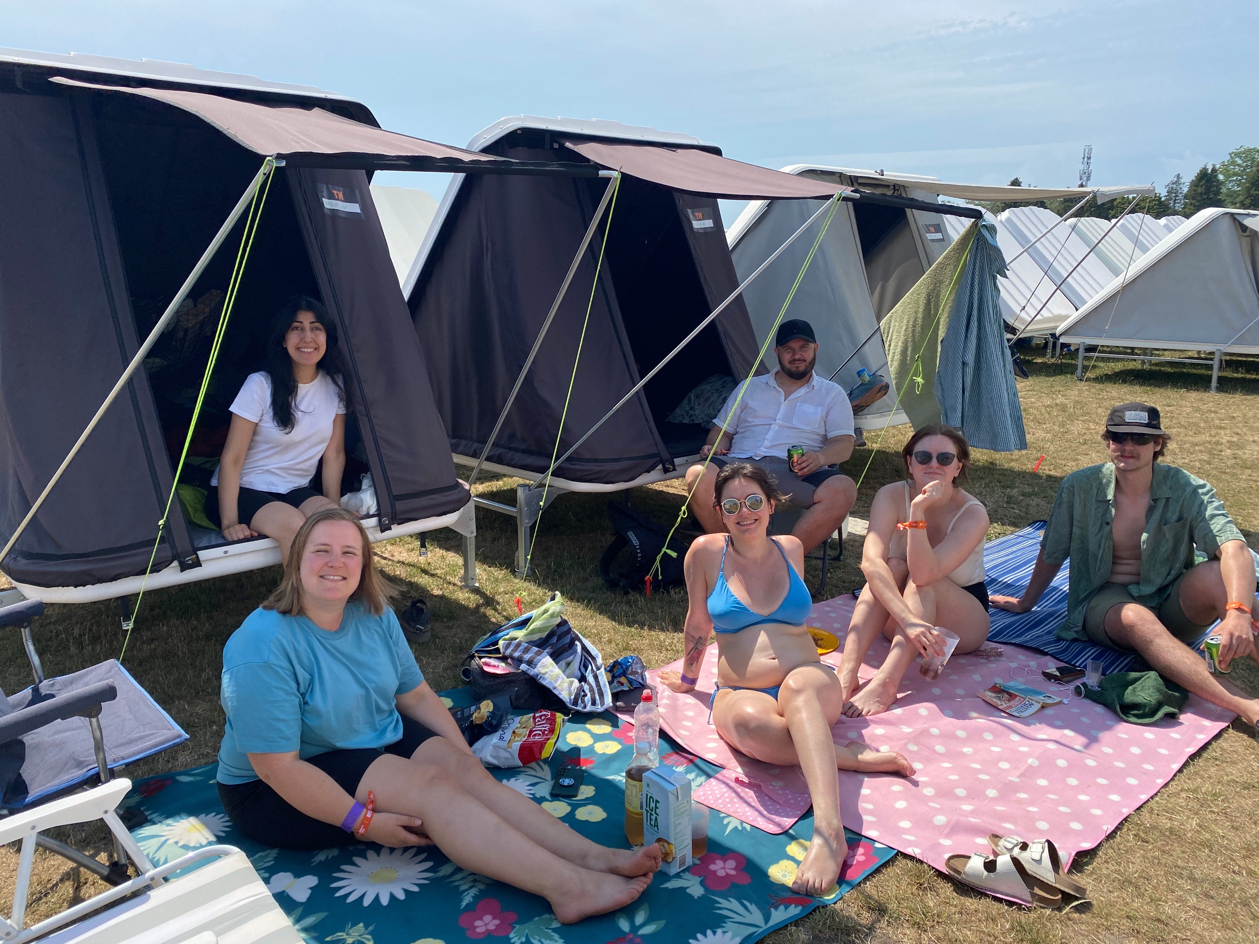 En gruppe norske venner er tilbage på Roskilde Festival efter flere års pause. De har valgt at betale ekstra for at bo i en slags faste campletter. Kristin Soli Hoff sidder forrest til venstre, mens Maria Magnusdottir sidder i midten på det lyserøde tæppe. Foto: Britt Nielsen