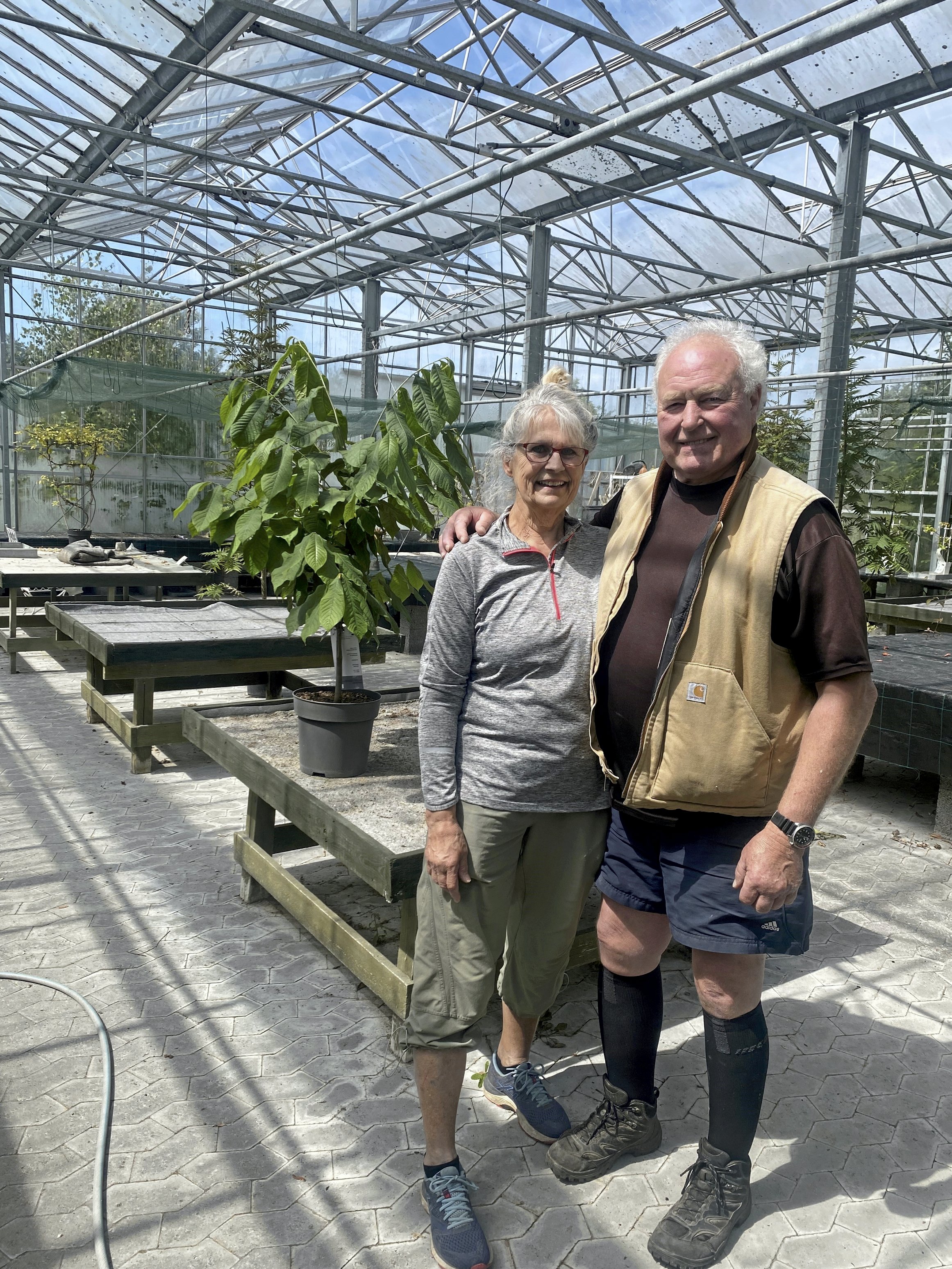Indehavere af Gilleleje Planteskole, Winnie og Patrick Watts, foran tomme planteborde, hvor der snart er helt udsolgt. Om kort tid takker helt af efter godt 25 gode år med forretningen, som har været deres livsværk. Foto: Anne Mette Ahlgreen