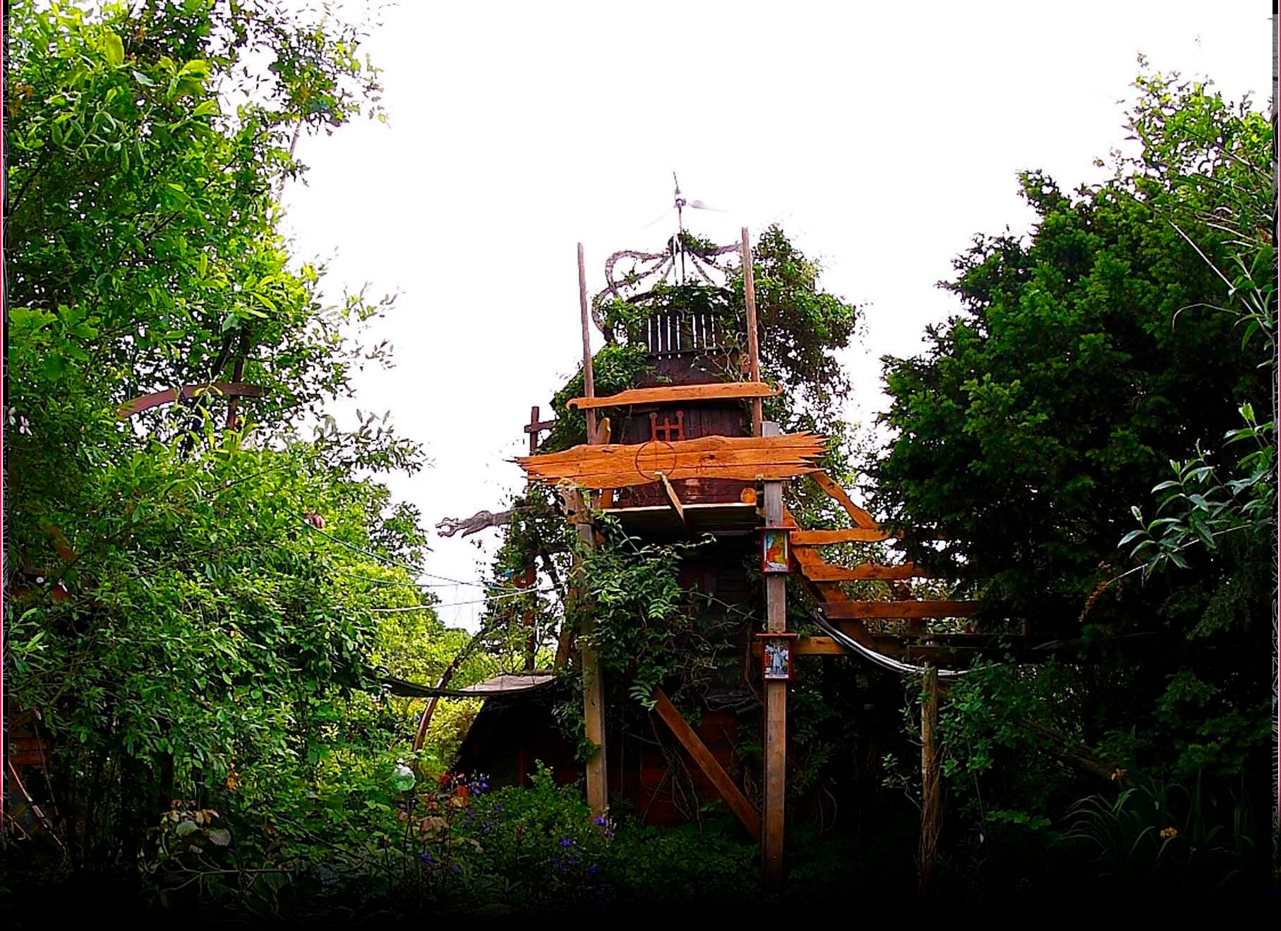 Længere bag i gården står et tårn og en scene mellem træer. Det hele er pyntet til med diverse symboler og stemningsskabende genstande. Foto: The Magic Garden