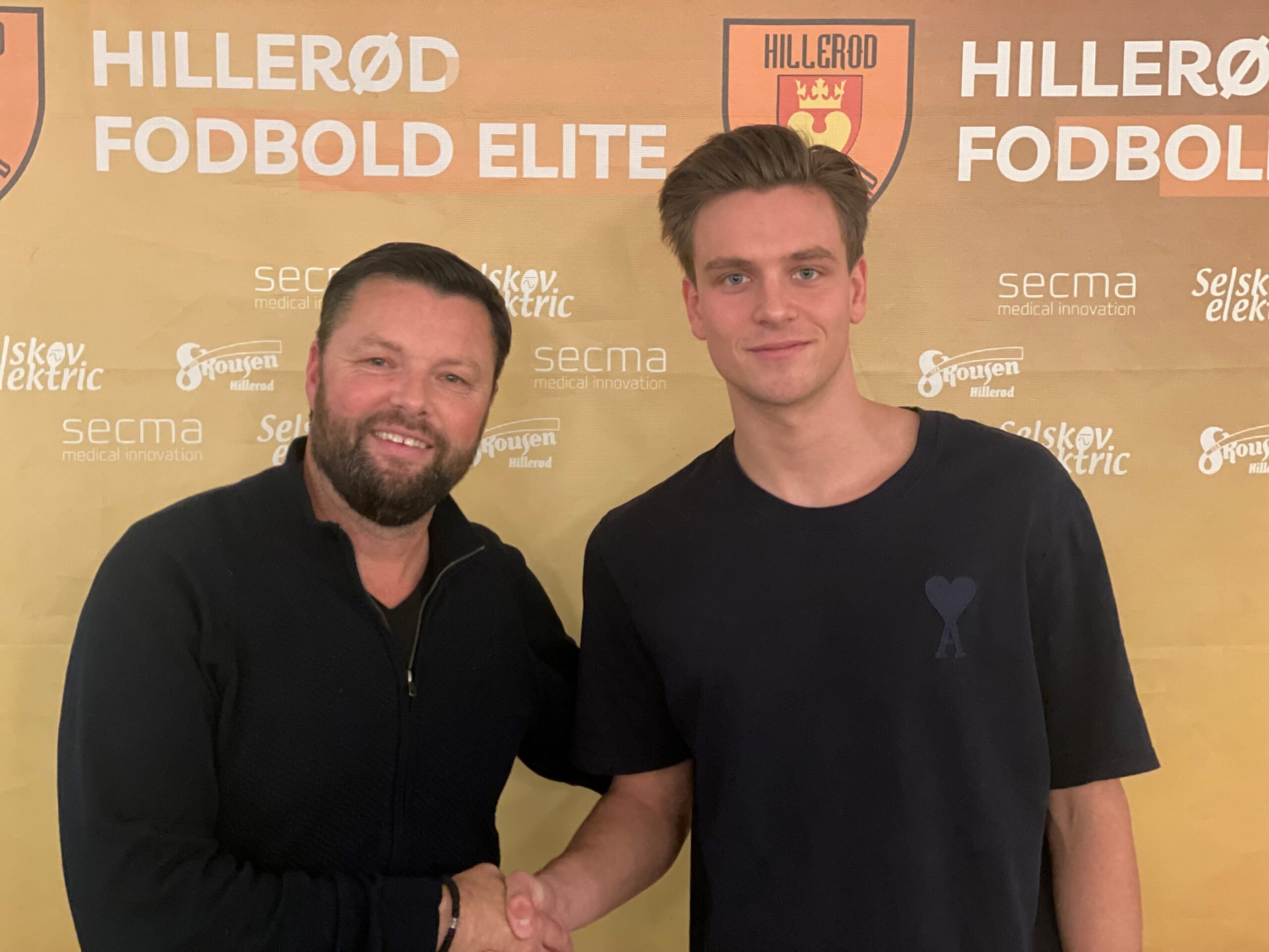 Christian Lønstrup og forsvarsspilleren Mads-Emil Langberg giver håndslag på at fortsætte samarbejdet til sommeren 2024. Foto: Hillerød Fodbold